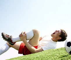 a man wearing a soccer uniform, laying on his back in a grass field, and holding his left calf in pain